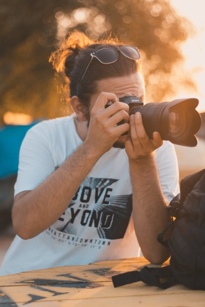 Young man using a DSLR camera to capture the sunset outdoors. Perfect scene for photography enthusiasts.