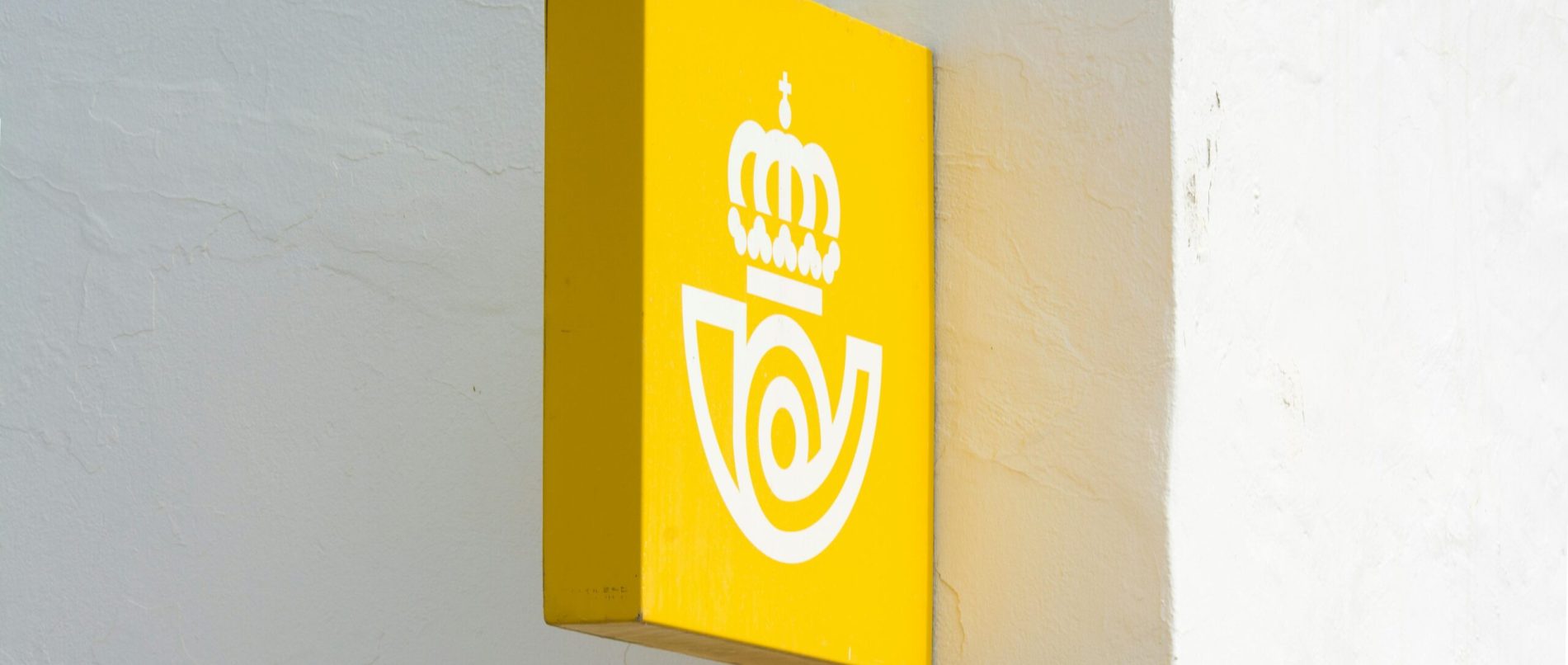 A striking yellow sign featuring a crown logo attached to a white wall, with clear, minimalistic design.